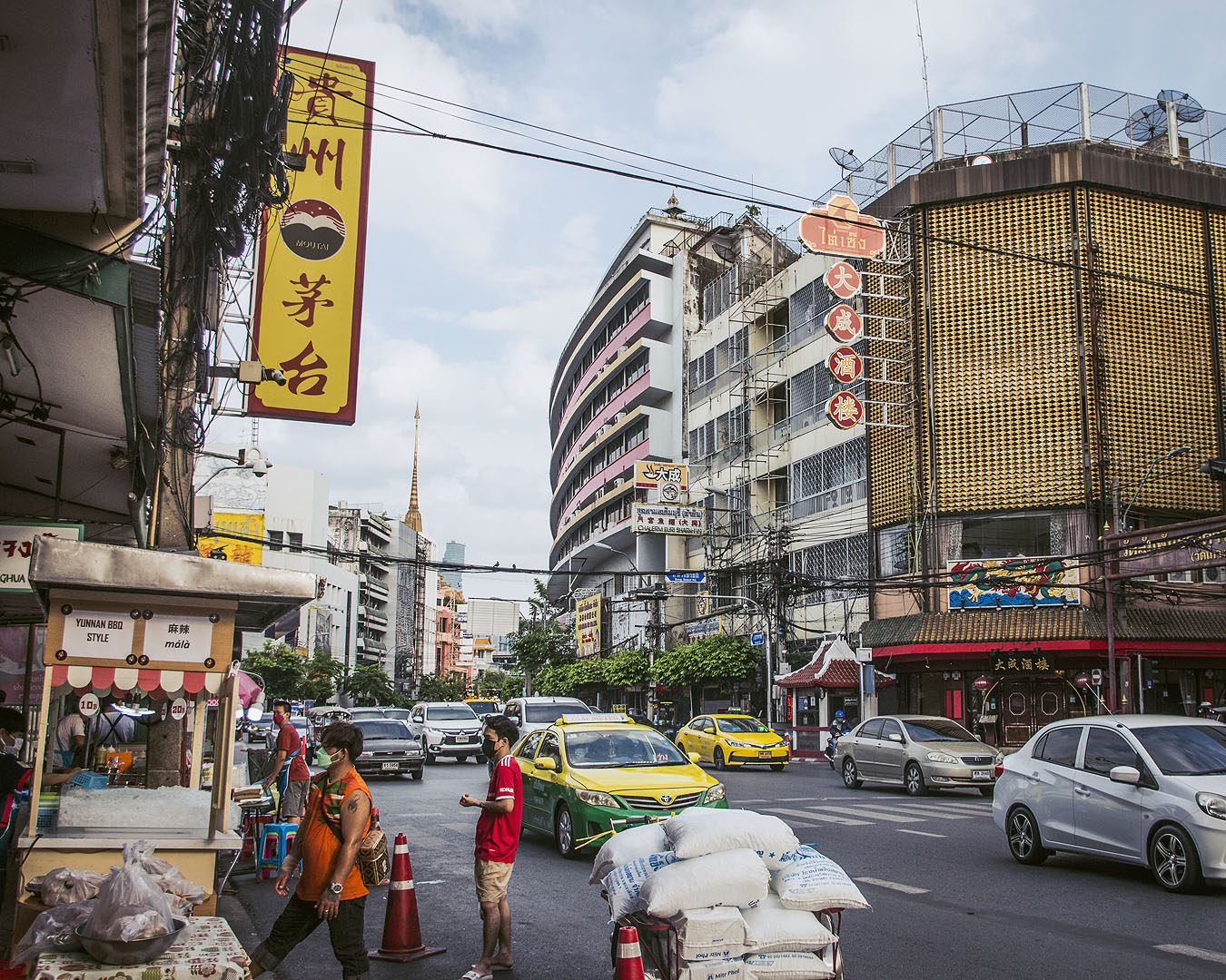 Taxis, pedestrians and store signs on Yaoworat Road in Bangkok's Chinatown, with a temple's chedi in the distance.