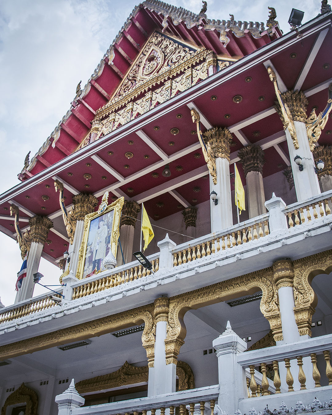 Looking up at the white and gold balustrades and red roof of Wat Samphanthawong.