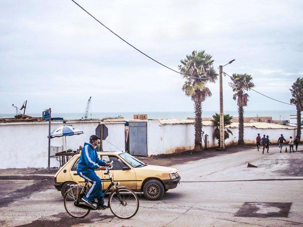 A taxi and man on a bike in front of white walls in Salé, Morocco.