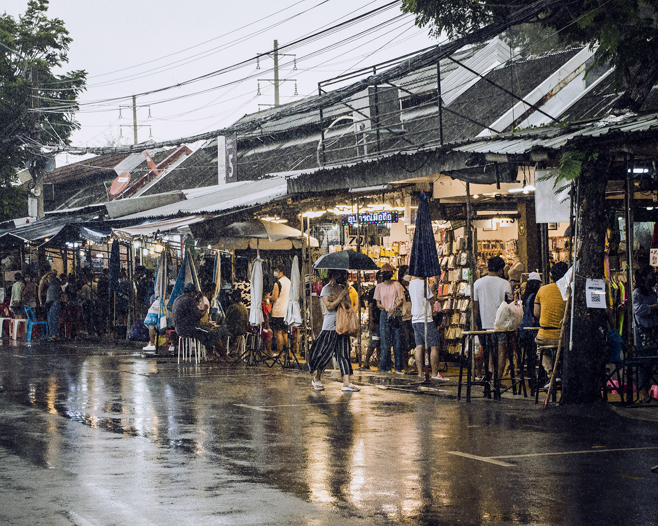 People browsing wares on a rainy street in Chatuchak Weekend Market.