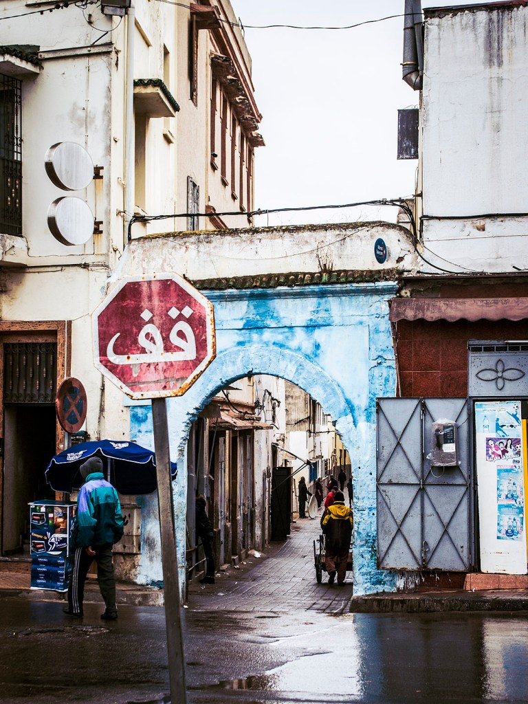 A stop sign in front of a blue arch on a rainy street in Salé, Morocco.