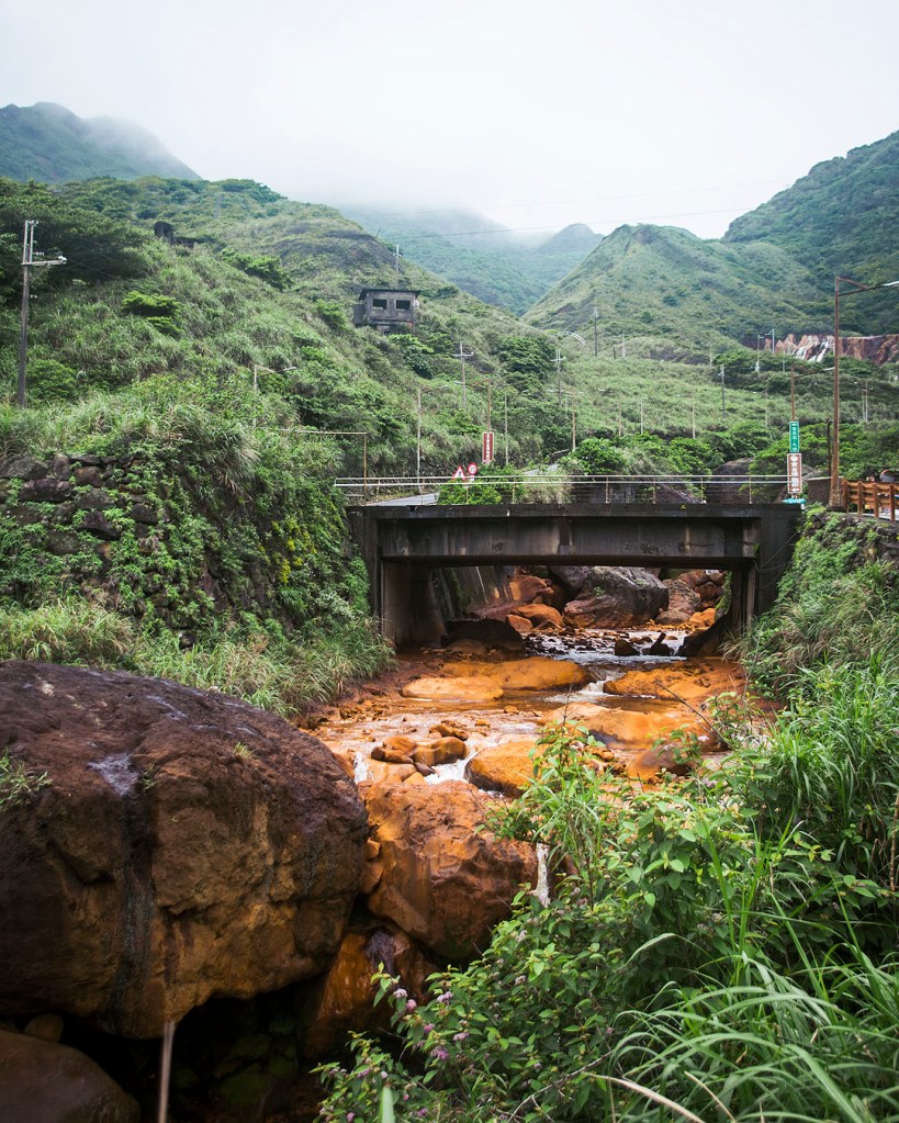 A bridge over the golden river, surrounded by green hills, near Jiufen, Taiwan.
