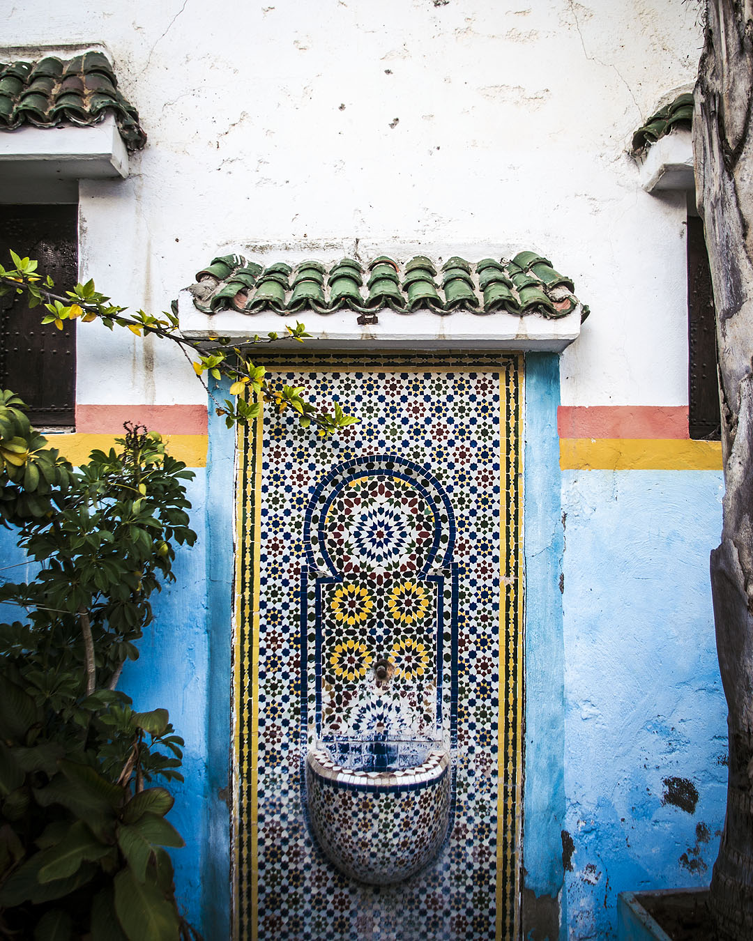 A traditional tiled fountain set into a blue, pink and yellow wall in the Kasbah of the Udayas.