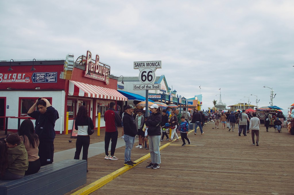 The end of Route 66 sign on the crowded Santa Monica Pier on a cloudy day.