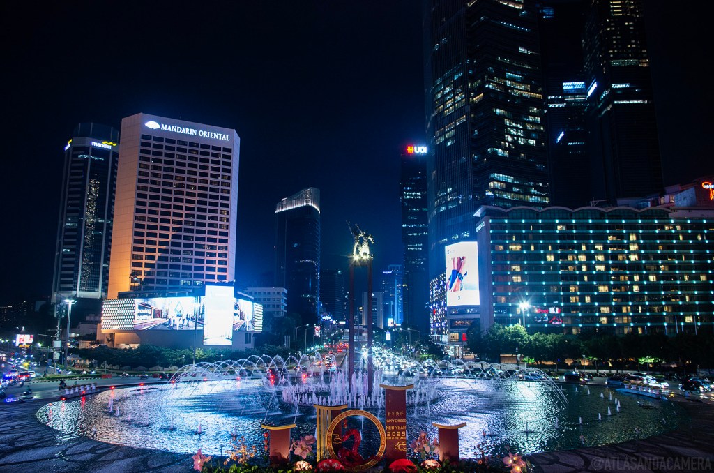 The view of a round fountain and illuminated skyscrapers from Bundaran HI in Jakarta.