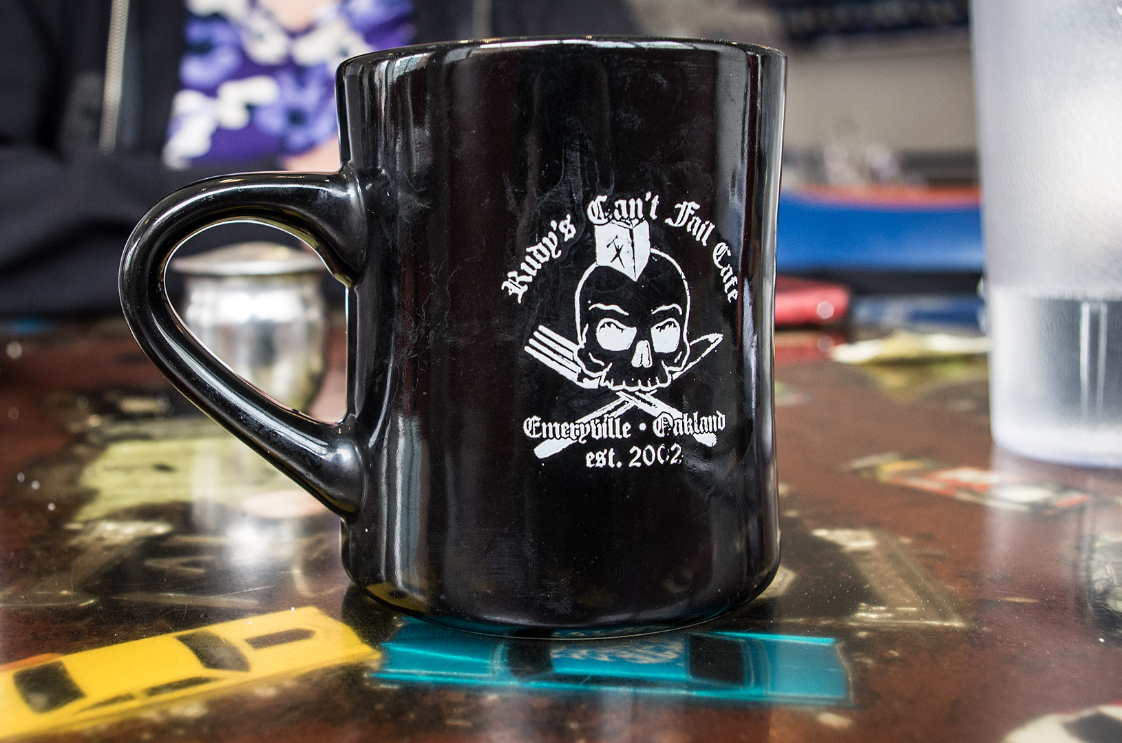 A black Rudy's Can't Fail Cafe mug with a white skull and crossbones logo.