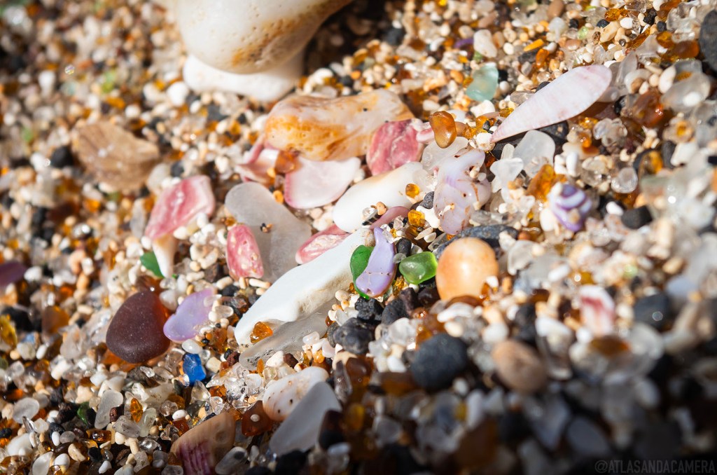 A close-up photo of shards of sea glass in blue, lilac, pink, green, white and black on the Glass Beach on Kauai.